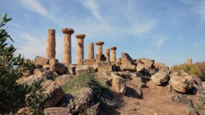 Vista della Valle dei Templi di Agrigento al tramonto, con antiche colonne illuminate da calde tonalità arancioni.