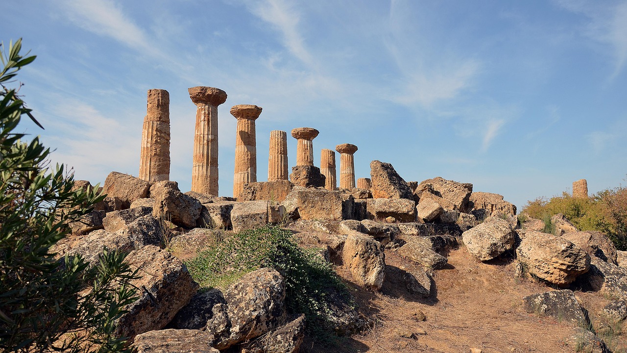 Vista della Valle dei Templi di Agrigento al tramonto, con antiche colonne illuminate da calde tonalità arancioni.
